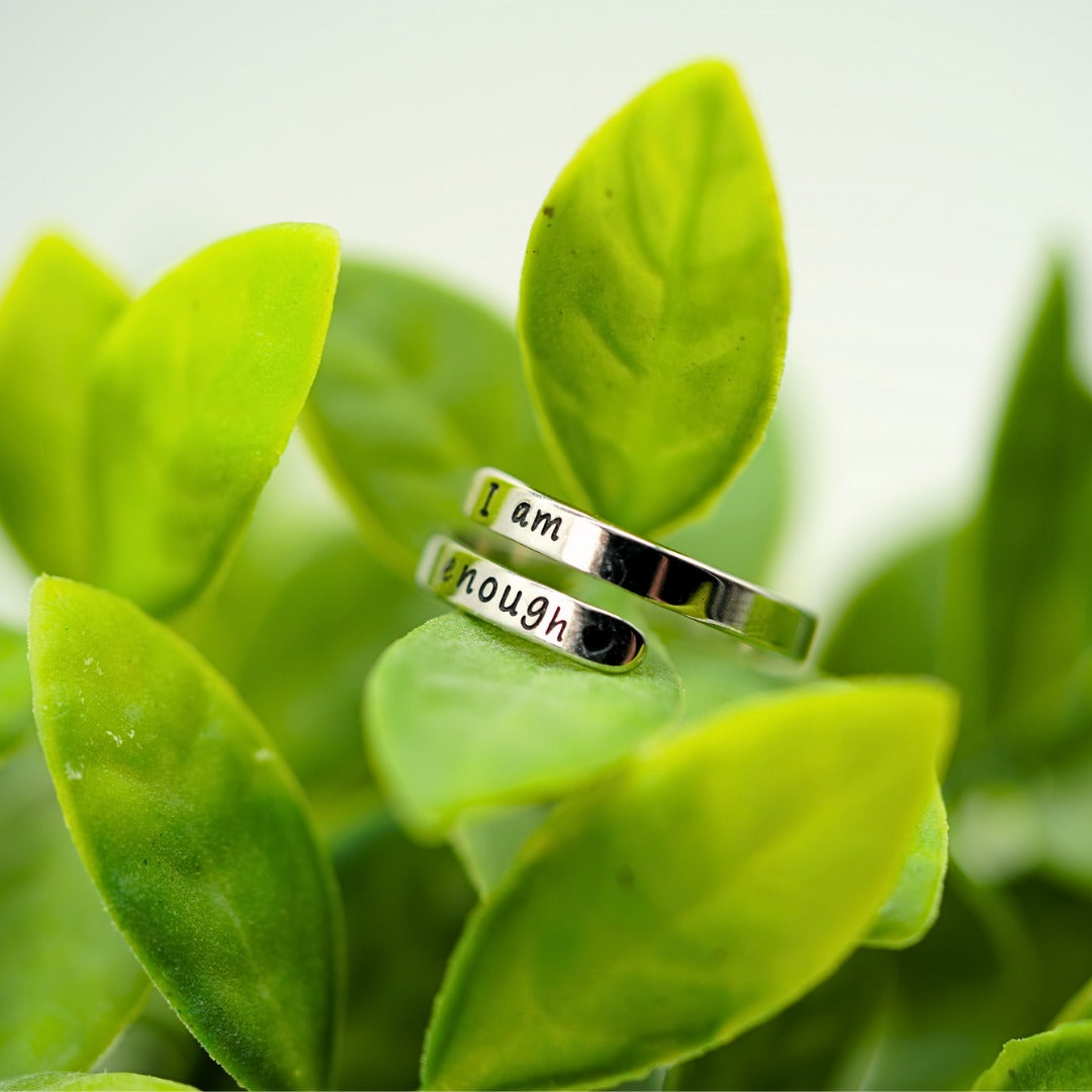 I Am Enough wrap ring resting on green leaves
